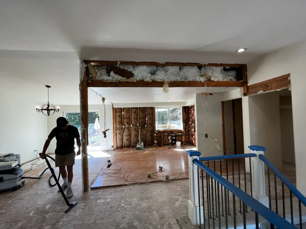 Home Run Design Remodel team member vacuums floor in a house renovation showing exposed wall framing and insulation installation.