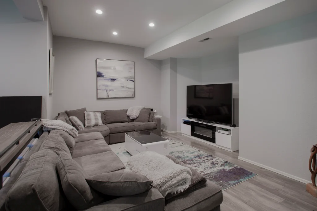 Home Run Design Remodel modern living room with gray sectional sofas, flat-screen TV, glass coffee table, area rug, and abstract art.