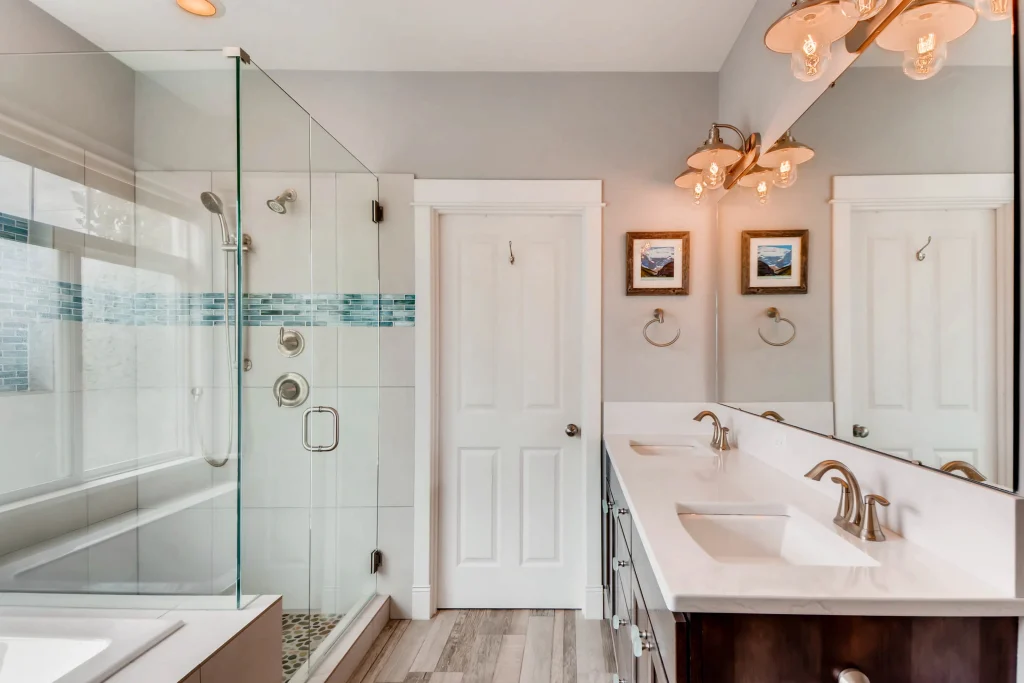 Modern bathroom remodel by Home Run Design Remodel featuring glass shower, dual sinks, large mirror, framed art, wood-look tile.