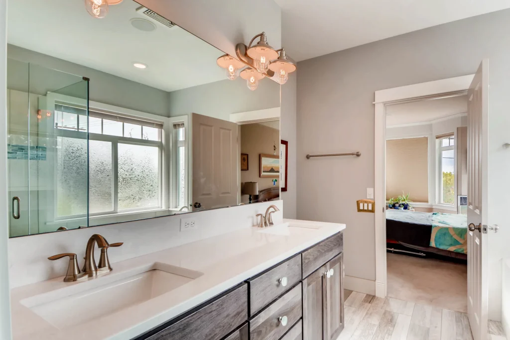 Home Run Design Remodel modern bathroom with double sink vanity, large mirror, brushed nickel fixtures, and open bedroom view.