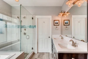 Bright contemporary bathroom with a glass-enclosed shower, double vanity, and two framed landscape pictures on the wall near the mirror.